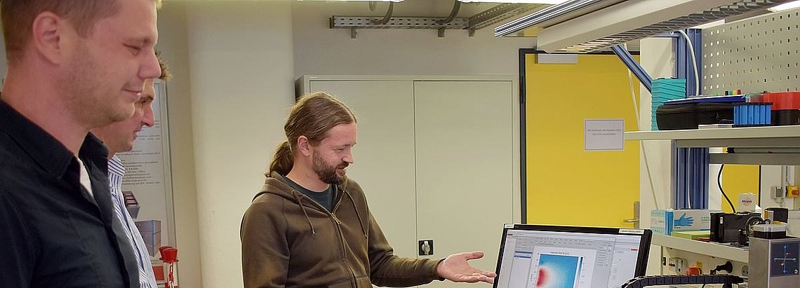 Personen, die nebeneinander stehen, wobei eine Person auf einen Bildschirm zeigt