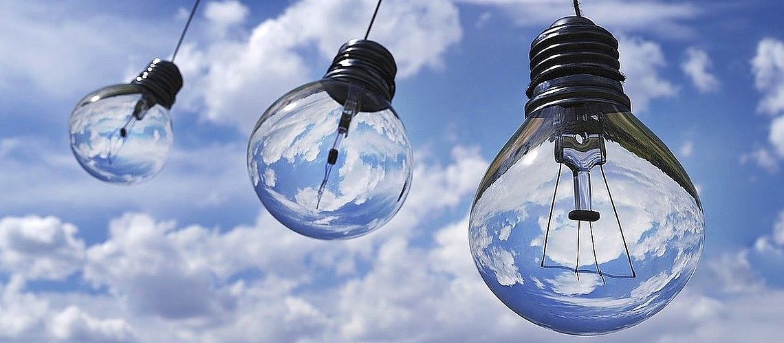 drei Mini-Glühbirnen hängen in der Luft mit blauem Himmel mit Wolken im Hintergrund