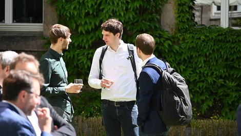 Mensch sind im Gespräch. Sie stehen in einem begrünten Innenhof.