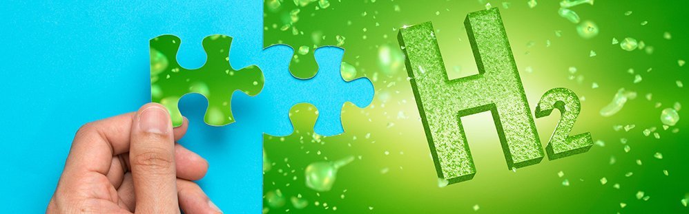 Eine Hand hält ein grünes Puzzleteil. Daben befindet sich ein angefangenes grünes Puzzle mit der Aufschrift H2.