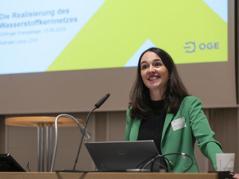 Eine Frau mit dunklen Haaren und grünem Obertei steht an einem Mikrofon. 