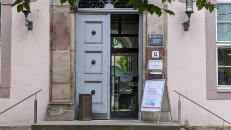 Eine Tür, deren eine Seite offen ist. daneben steht ein Aufsteller. Er weist auf eine Tagung hin.
