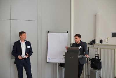 Die Person am Rednerpult hält eine Präsentation, während eine andere Person an der Seite steht