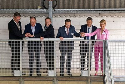 Sechs Personen stehen nebeneinander, wobei jeweils drei Personen einen Knopf drücken