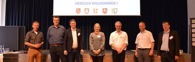 Eine Gruppe von Personen stehen nebeneinander vor einer Leinwand