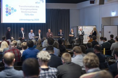 mehrere Männer und eine Frau an Tischen vor dem Plenum
