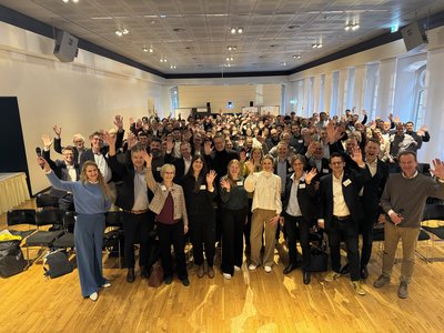 Zahlreiche Menschen stehen in einem Raum und winken.