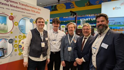 Menschen an einem Messestand neben einem Exponat