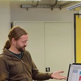 Personen, die nebeneinander stehen, wobei eine Person auf einen Bildschirm zeigt
