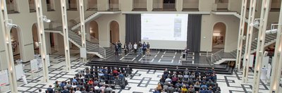 Teilnehmer eines Seminars und Personen stehen auf der Bühne vor der Projektionsfläche 