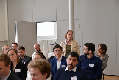 Personen nehmen an einer Veranstaltung teil, bei der alle sitzen, außer einer Person, die steht