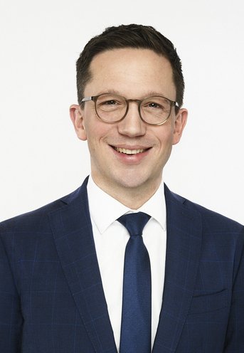 Porträtfoto von Falko Mohrs. Er hat dunkle Haare, eine Brille und lächelt